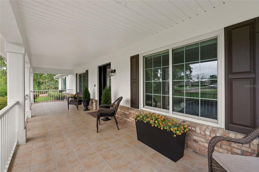 A covered porch features tiled flooring, brick accents, outdoor seating, and a large window — 5402 NW 76TH COURT, OCALA, FL