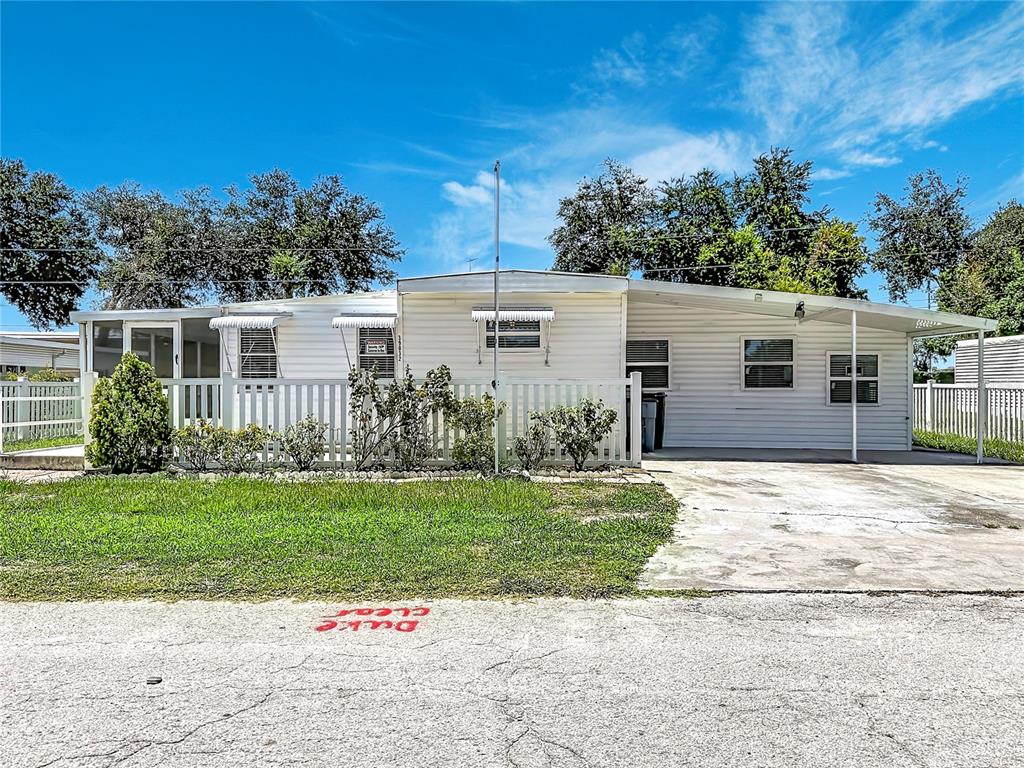 A single-story mobile home with white siding, a front porch, and an attached carport — 39032 OLA AVENUE, ZEPHYRHILLS, FL