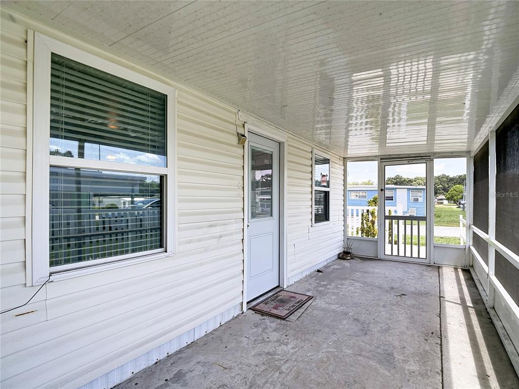 A covered porch with white siding, a screen door, and a concrete floor — 39032 OLA AVENUE, ZEPHYRHILLS, FL
