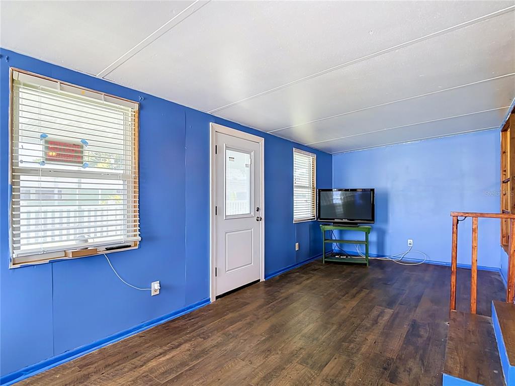 A room with blue walls, dark wood-look flooring, a white door, and a television — 39032 OLA AVENUE, ZEPHYRHILLS, FL