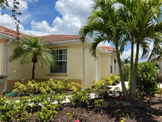 The exterior of a light yellow house features a tiled roof and palm trees — 3181 MATECUMBE KEY ROAD UNIT 34, PUNTA GORDA, FL
