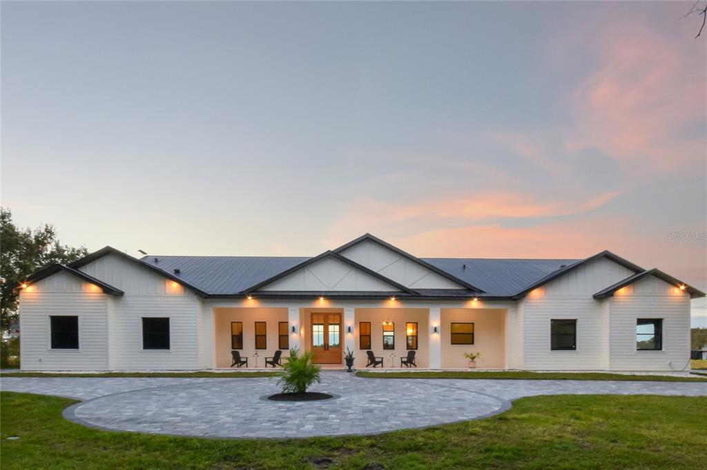 A modern white farmhouse with a metal roof and a circular paver driveway at dusk — 4940 WAUCHULA ROAD, MYAKKA CITY, FL