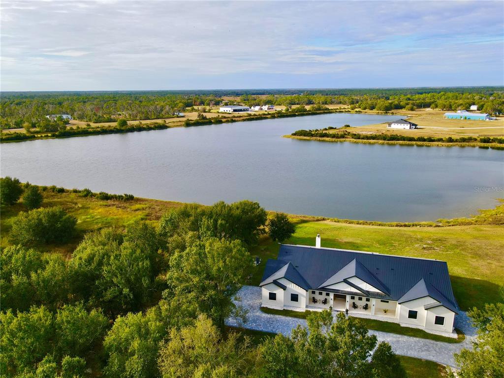 An aerial view shows a modern house with a dark roof situated beside a lake — 4940 WAUCHULA ROAD, MYAKKA CITY, FL