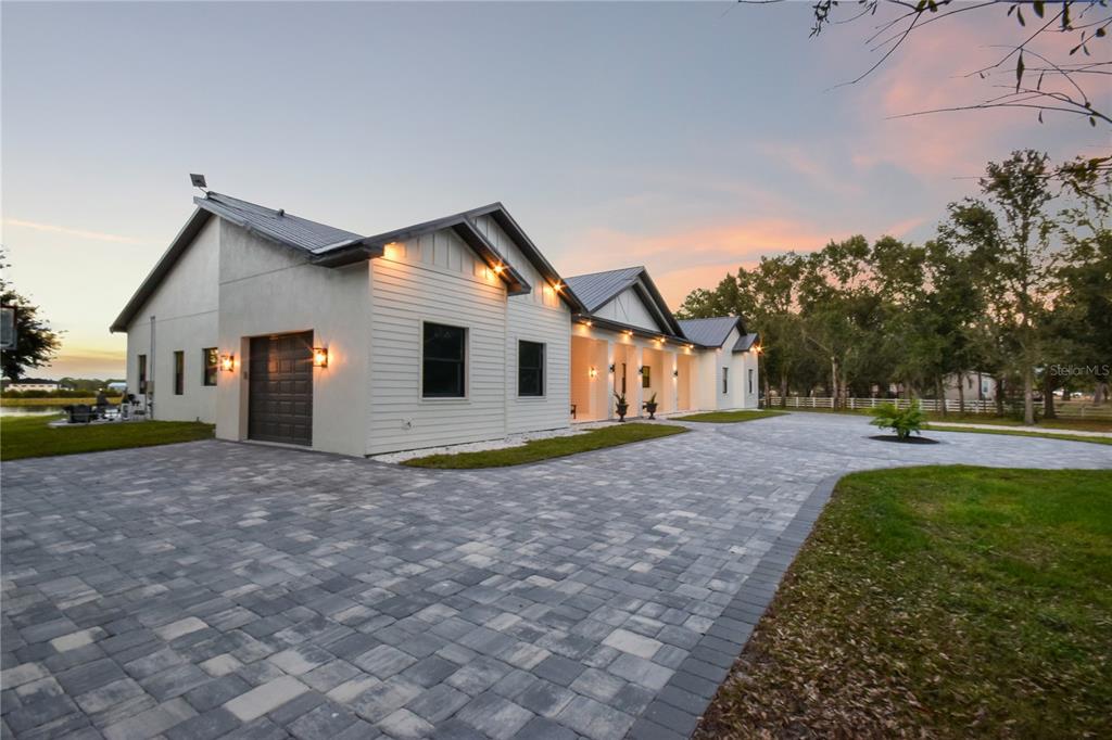 A modern white house with a metal roof and a large paver driveway at dusk — 4940 WAUCHULA ROAD, MYAKKA CITY, FL