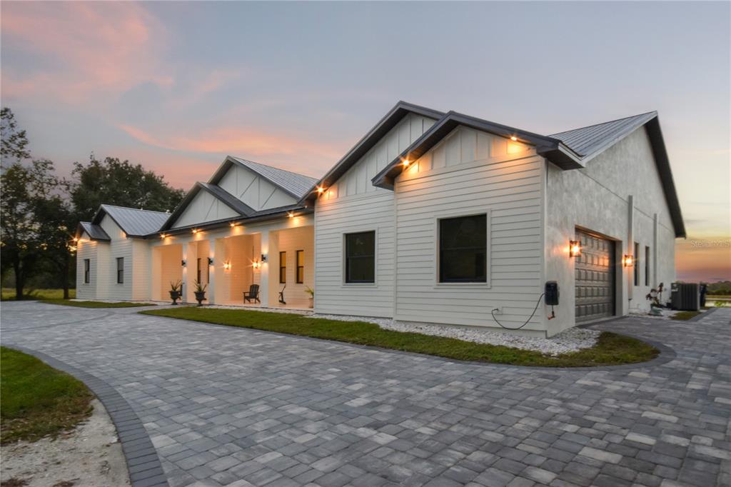 A modern white farmhouse with a metal roof and a large paver driveway at dusk — 4940 WAUCHULA ROAD, MYAKKA CITY, FL
