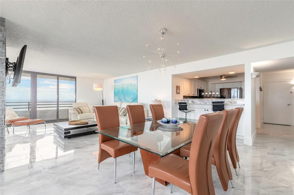 A dining area with a glass table and leather chairs opens to a living room — 1420 N ATLANTIC AVENUE UNIT 601, DAYTONA BEACH, FL