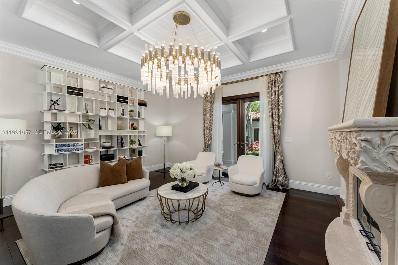 A living room features a coffered ceiling, a large chandelier, built-in shelving, and a fireplace — 12575 Pine Needle Ln, Pinecrest FL 33156, PINECREST, FL