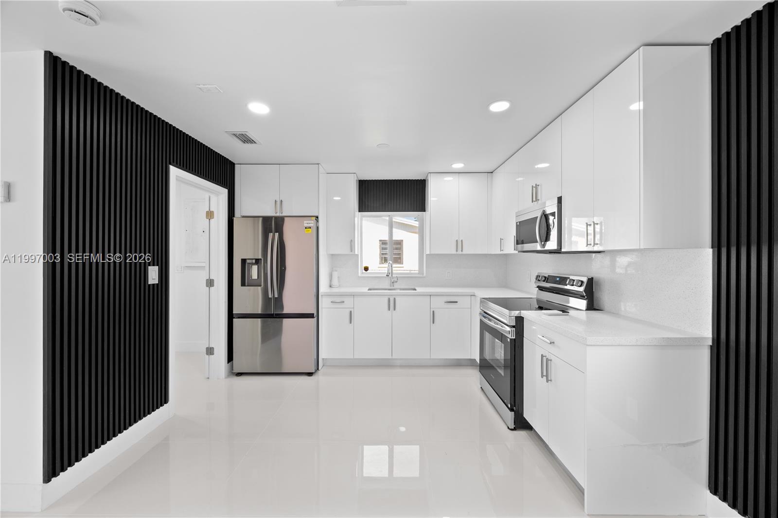 A modern kitchen features white cabinets, stainless steel appliances, and black vertical slat wall accents — 22503 SW 113th Pl, Miami FL 33170, MIAMI, FL