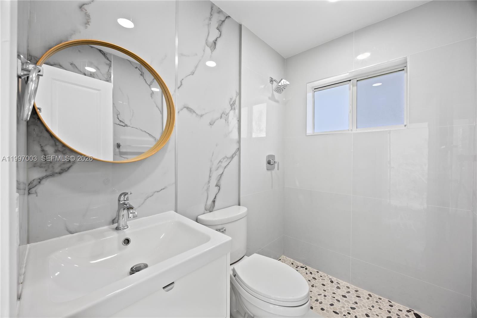 A modern bathroom features a white vanity, a round gold mirror, and marble-tiled walls — 22503 SW 113th Pl, Miami FL 33170, MIAMI, FL