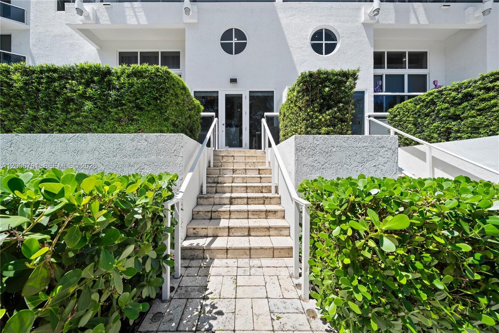 A white building exterior features a central staircase leading to a glass-paned entrance door — 400 Alton Rd # 1A, Miami Beach FL 33139, MIAMI BEACH, FL
