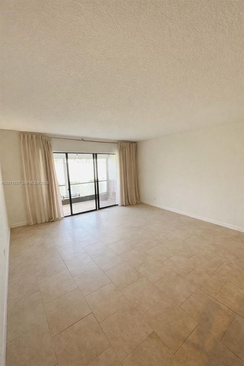 An empty living room features beige tile flooring, white walls, and sliding glass balcony doors — 1110 Green Pine Blvd # C1, West Palm Beach FL 33409, WEST PALM BEACH, FL