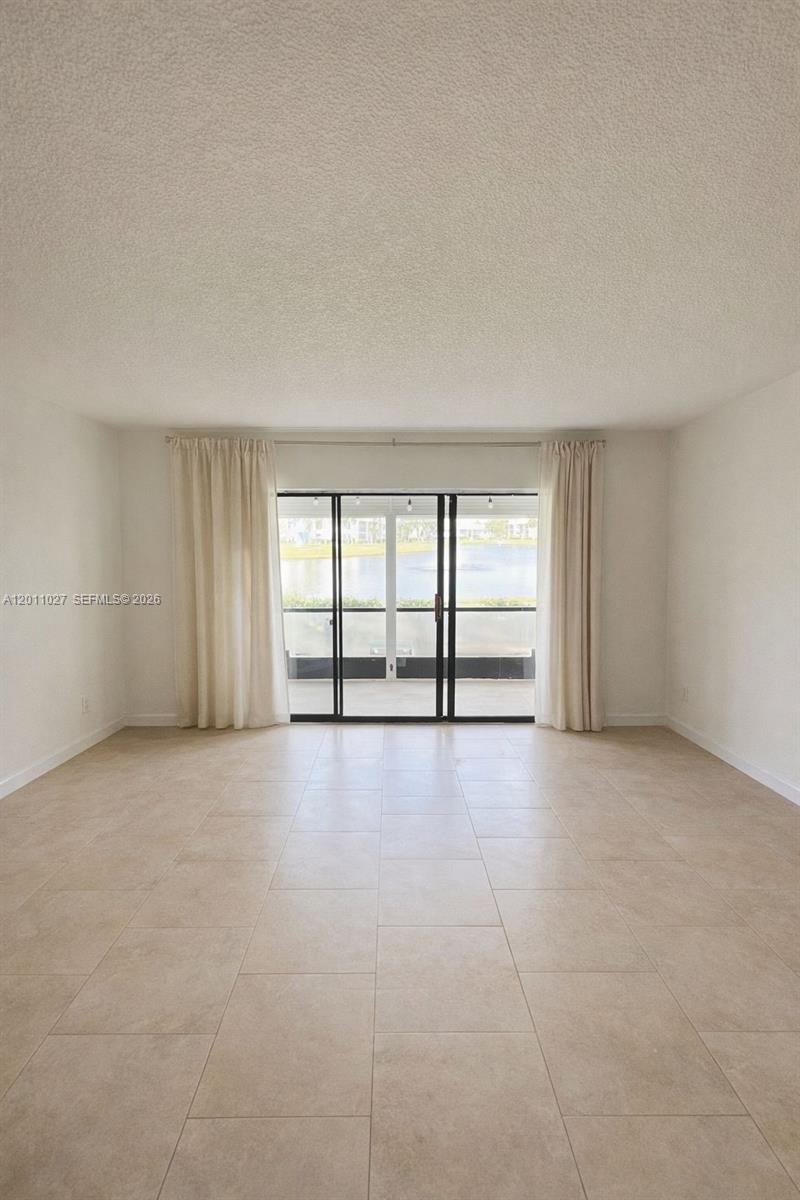 A living room with light-colored tile flooring, white walls, and sliding glass doors to a balcony — 1110 Green Pine Blvd # C1, West Palm Beach FL 33409, WEST PALM BEACH, FL