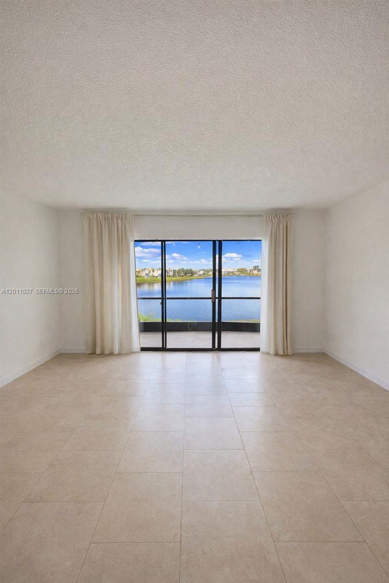 A bright, empty room features light tile flooring, white walls, and sliding glass doors overlooking water — 1110 Green Pine Blvd # C1, West Palm Beach FL 33409, WEST PALM BEACH, FL