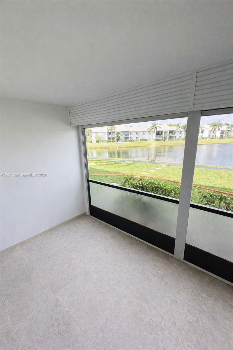 A sunroom with tiled flooring features large windows overlooking a lake and grassy area — 1110 Green Pine Blvd # C1, West Palm Beach FL 33409, WEST PALM BEACH, FL
