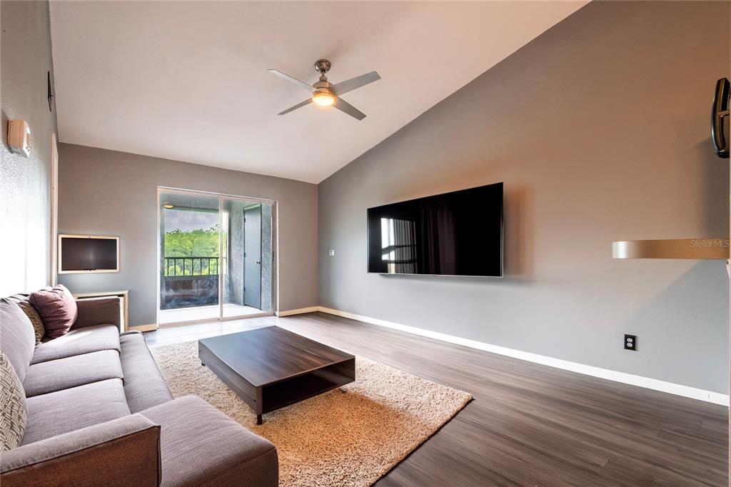 A living room features gray walls, wood-look flooring, a ceiling fan, and a wall-mounted television — 11201 122ND AVENUE UNIT 234, LARGO, FL