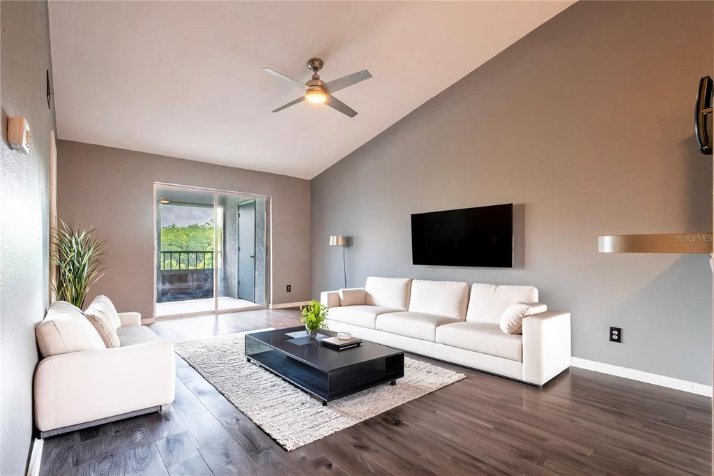 A living room features white sofas, a black coffee table, and a balcony with greenery — 11201 122ND AVENUE UNIT 234, LARGO, FL