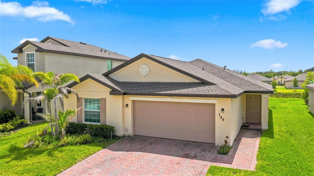 A single-story house with a beige stucco exterior, a two-car garage, and a brick driveway — 749 WORLINGTON LANE, FORT PIERCE, FL