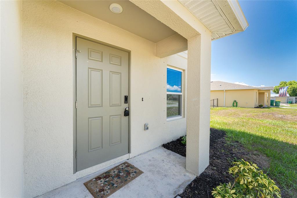 A beige exterior entryway features a light gray six-panel door and a concrete porch — 1550 PAXTON TERRACE, PORT CHARLOTTE, FL
