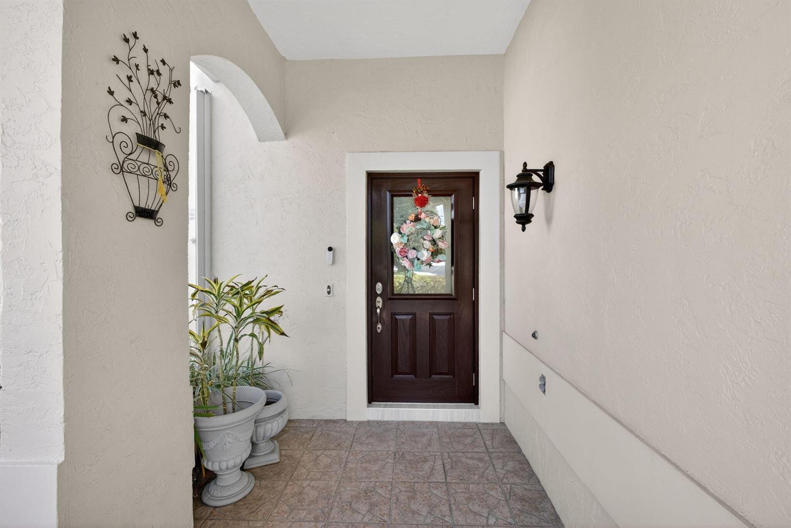 A covered entryway features a dark wood front door, tile flooring, and a wall sconce — 151 St Michaels Court, Jupiter FL 33458, JUPITER, FL