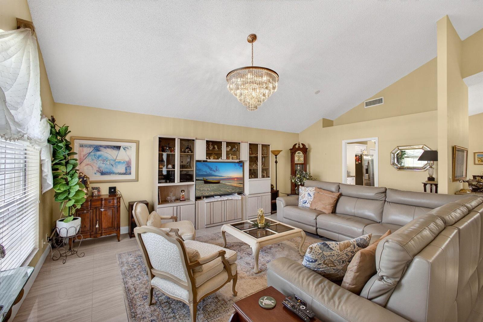 A living room features a vaulted ceiling, a crystal chandelier, and a large entertainment center — 151 St Michaels Court, Jupiter FL 33458, JUPITER, FL