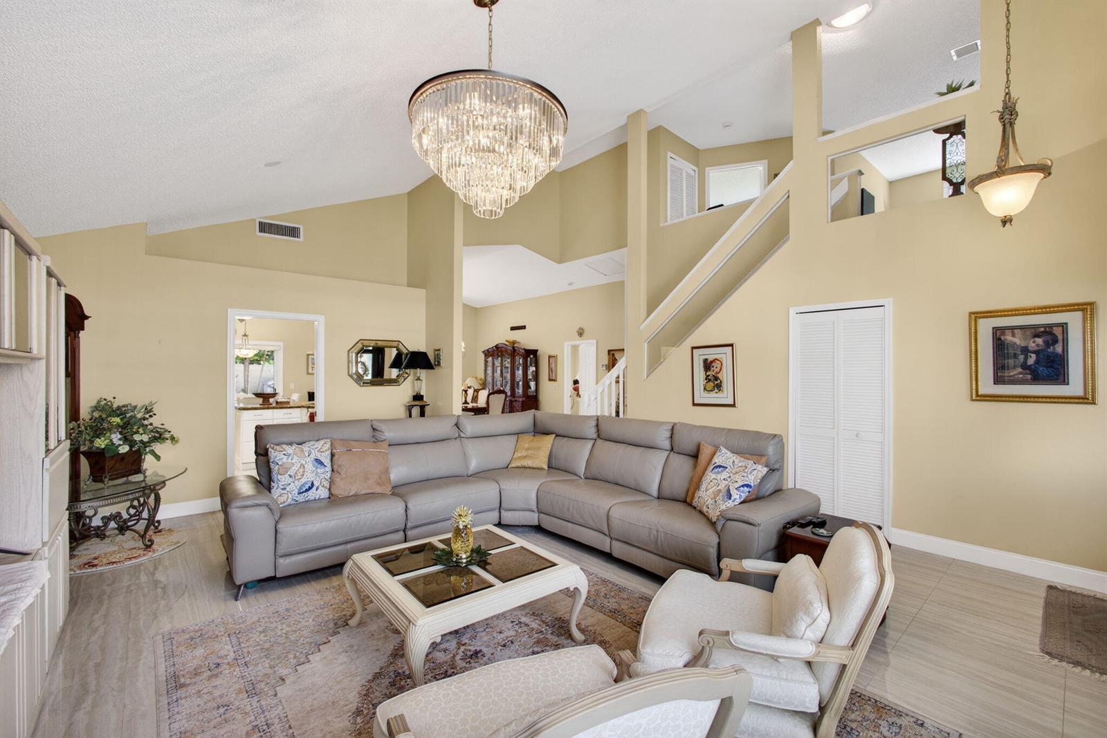 A living room features a large sectional sofa, a crystal chandelier, and vaulted ceilings — 151 St Michaels Court, Jupiter FL 33458, JUPITER, FL