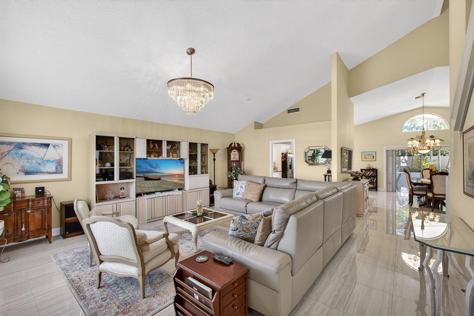 A living room with a vaulted ceiling, light tile floors, and a large sectional sofa — 151 St Michaels Court, Jupiter FL 33458, JUPITER, FL