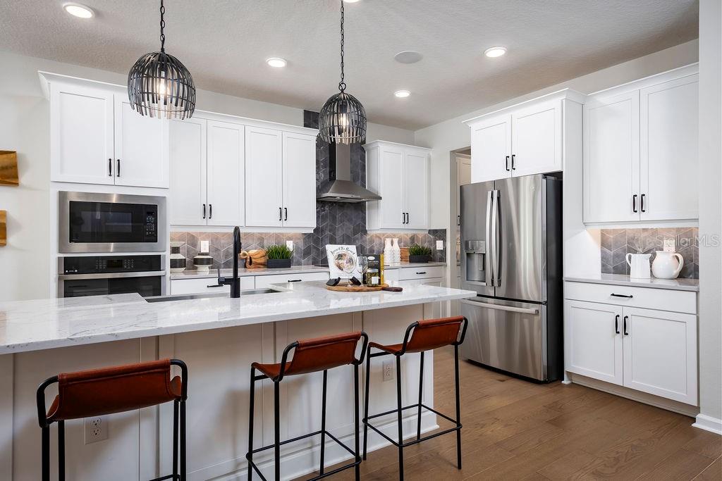 A modern kitchen features white cabinetry, a marble-topped island, stainless steel appliances, and pendant lighting — 1205 BASALT LANE, SANFORD, FL