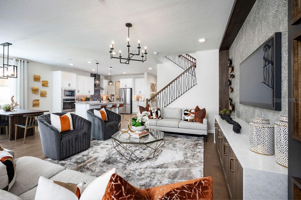 An open-concept living room and kitchen featuring a gray sofa, two armchairs, and a staircase — 1205 BASALT LANE, SANFORD, FL