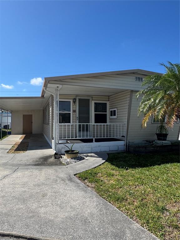 A single-story manufactured home with a concrete driveway, carport, and a small front porch — 118 52ND AVENUE W, BRADENTON, FL