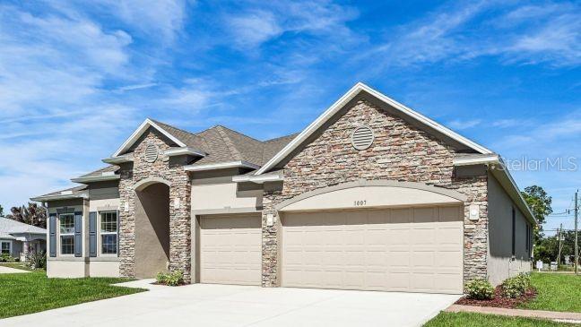 A single-story house exterior features a stone facade, a three-car garage, and a blue sky — 12990 STILLWATER COVE DRIVE, ASTATULA, FL
