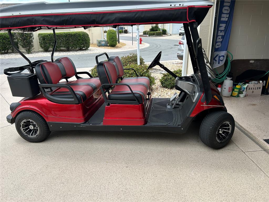 A red four-passenger golf cart with black trim is parked on a concrete driveway — 7809 SE 171ST HARLESTON STREET, THE VILLAGES, FL