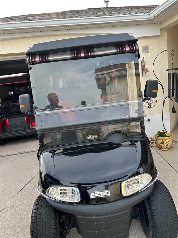 A black EZGO golf cart is parked on a concrete driveway in front of a house — 7809 SE 171ST HARLESTON STREET, THE VILLAGES, FL