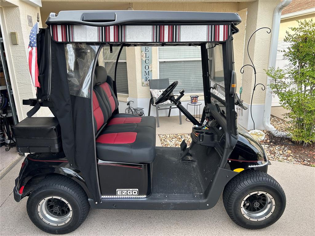 A black EZGO golf cart with red and black seats parked on a residential driveway — 7809 SE 171ST HARLESTON STREET, THE VILLAGES, FL