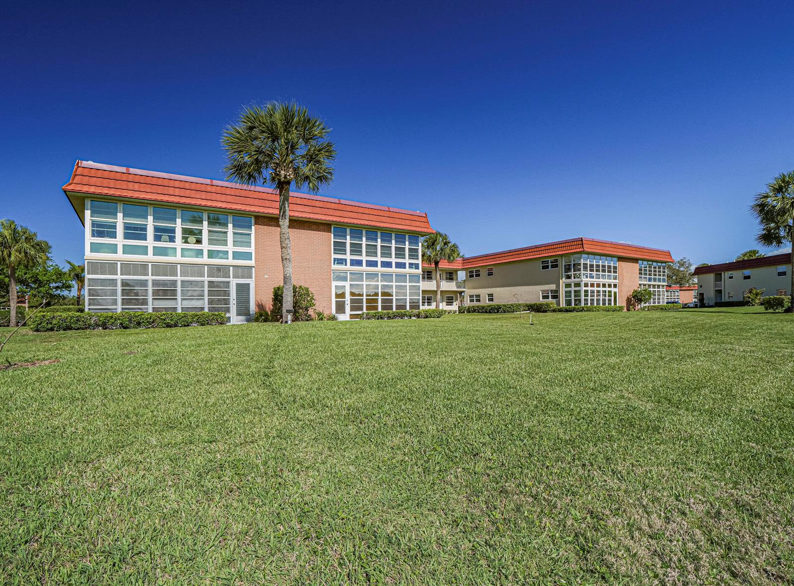 A multi-story apartment building with a red roof sits behind a large, grassy lawn — 67 Royal Oak Drive # 206, Vero Beach FL 32962, VERO BEACH, FL