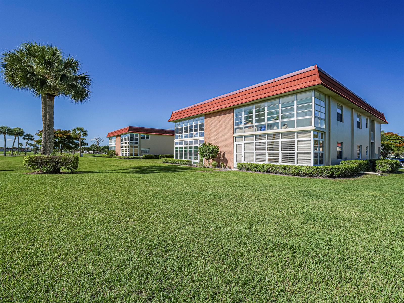 Exterior view of two multi-story apartment buildings with red roofs and large windows on a lawn — 67 Royal Oak Drive # 206, Vero Beach FL 32962, VERO BEACH, FL