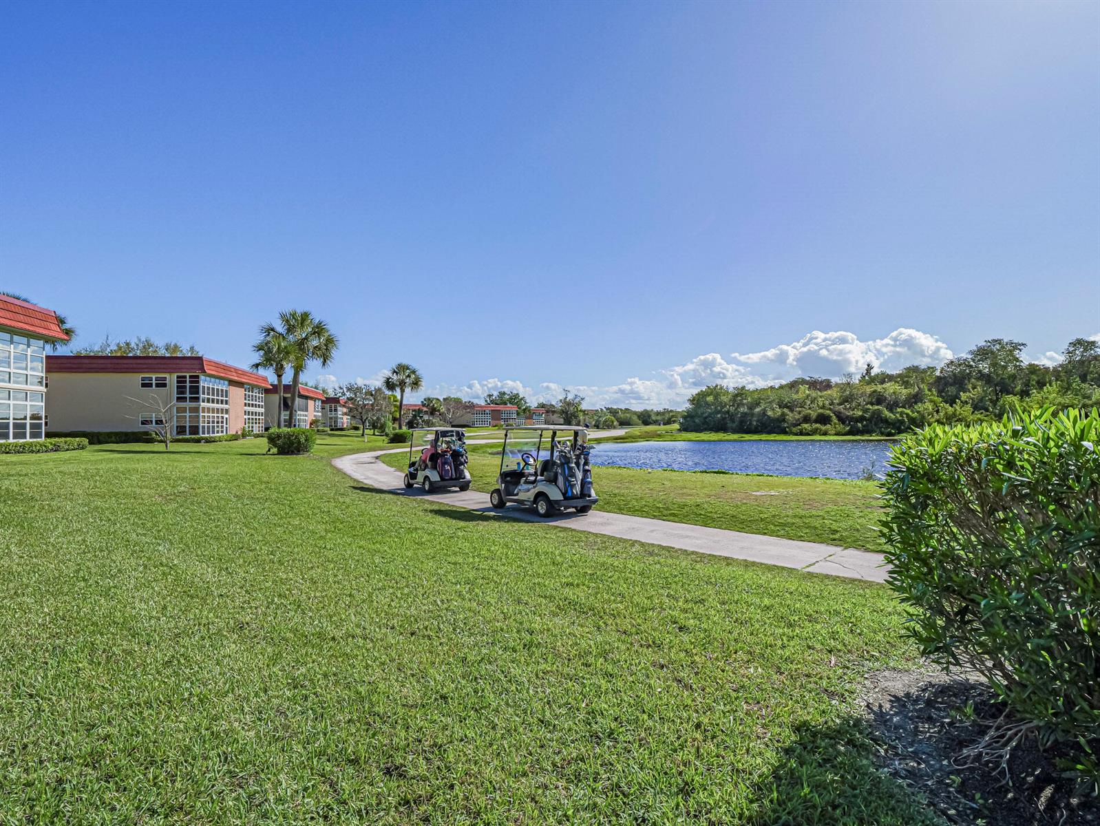 Two golf carts drive along a paved path beside a pond and apartment buildings — 67 Royal Oak Drive # 206, Vero Beach FL 32962, VERO BEACH, FL