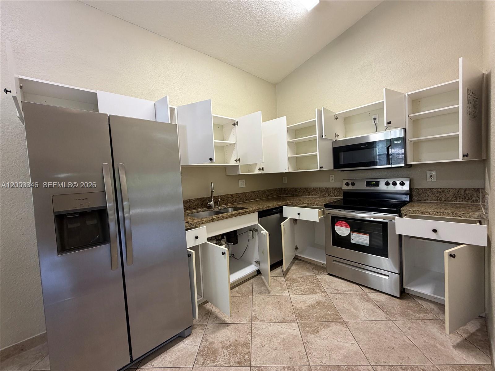 A kitchen with stainless steel appliances, granite countertops, and white cabinets with open doors — 5855 Eagle Cay Ter, Coconut Creek FL 33073, COCONUT CREEK, FL