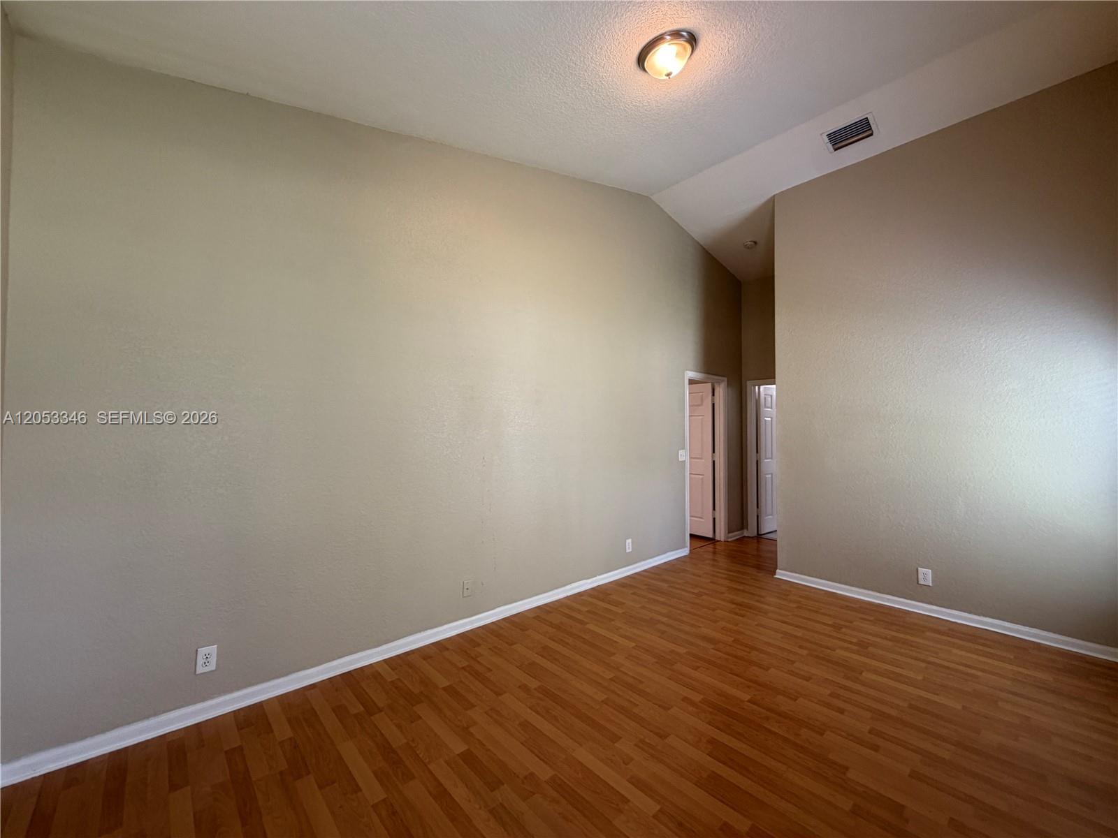 An empty room features vaulted ceilings, beige walls, and wood-look laminate flooring — 5855 Eagle Cay Ter, Coconut Creek FL 33073, COCONUT CREEK, FL
