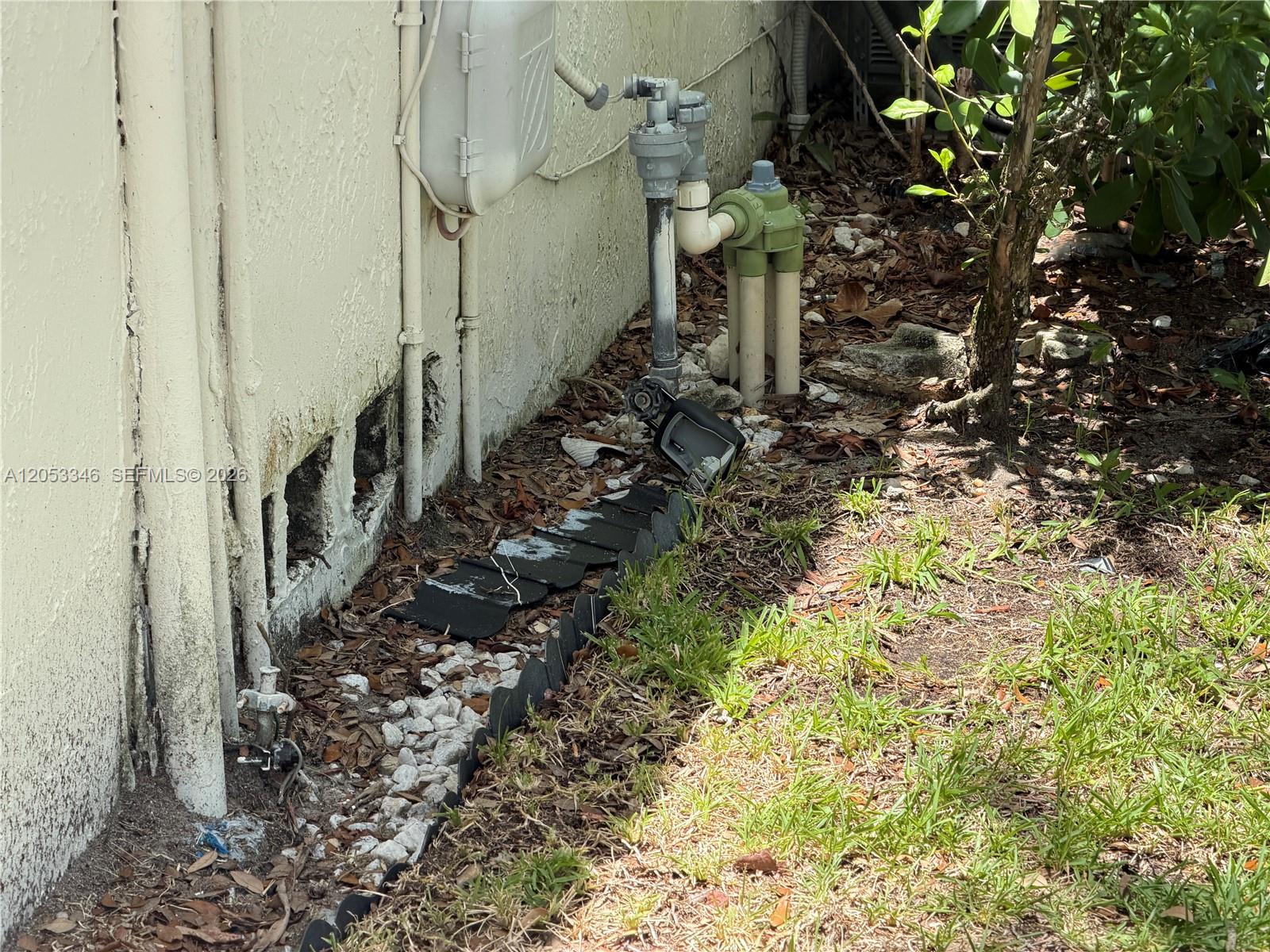 An exterior view shows a house wall with exposed foundation blocks, utility pipes, and landscaping — 5855 Eagle Cay Ter, Coconut Creek FL 33073, COCONUT CREEK, FL