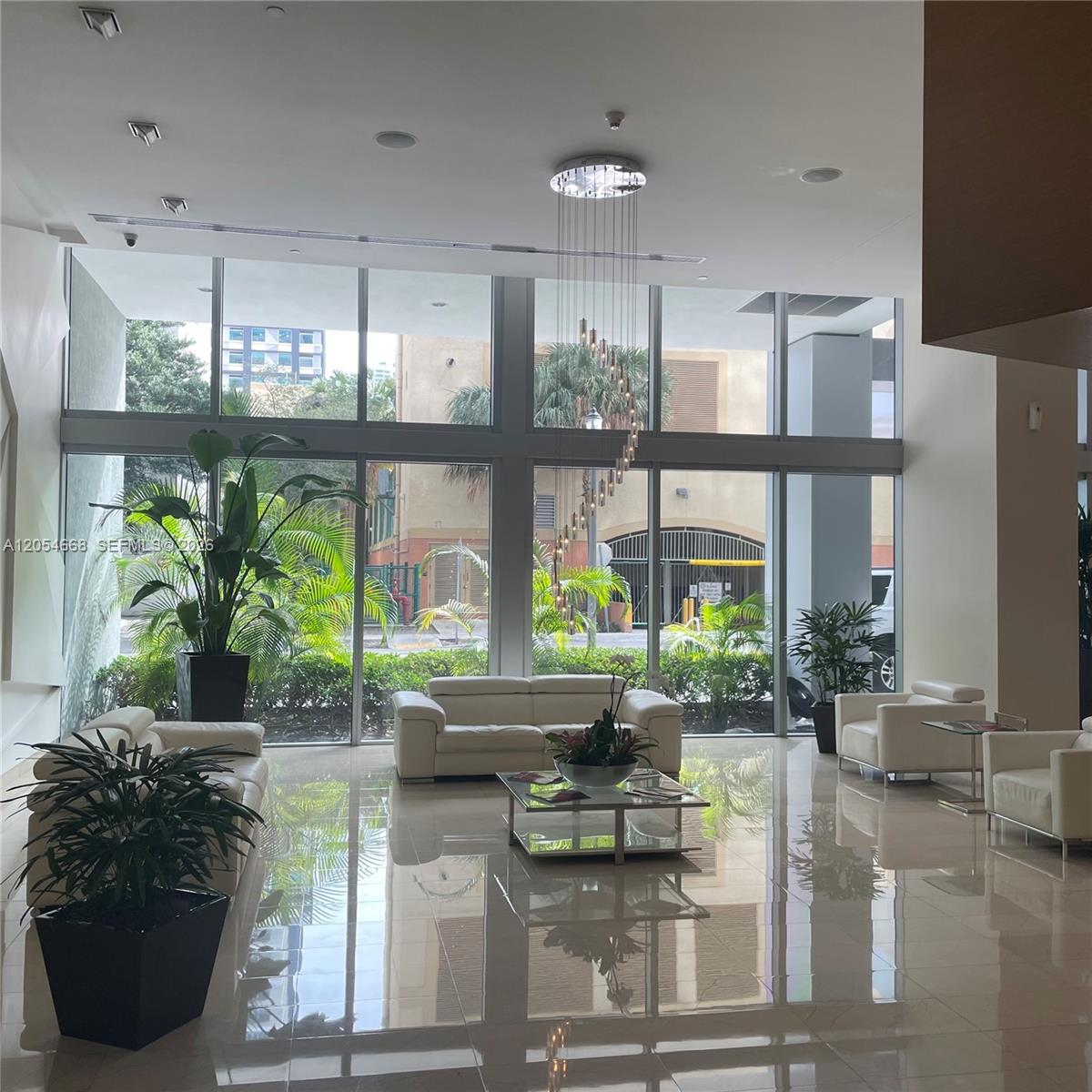 A modern lobby features white leather sofas, a glass coffee table, and floor-to-ceiling windows — 79 SW 12 ST, Miami FL 33130, MIAMI, FL