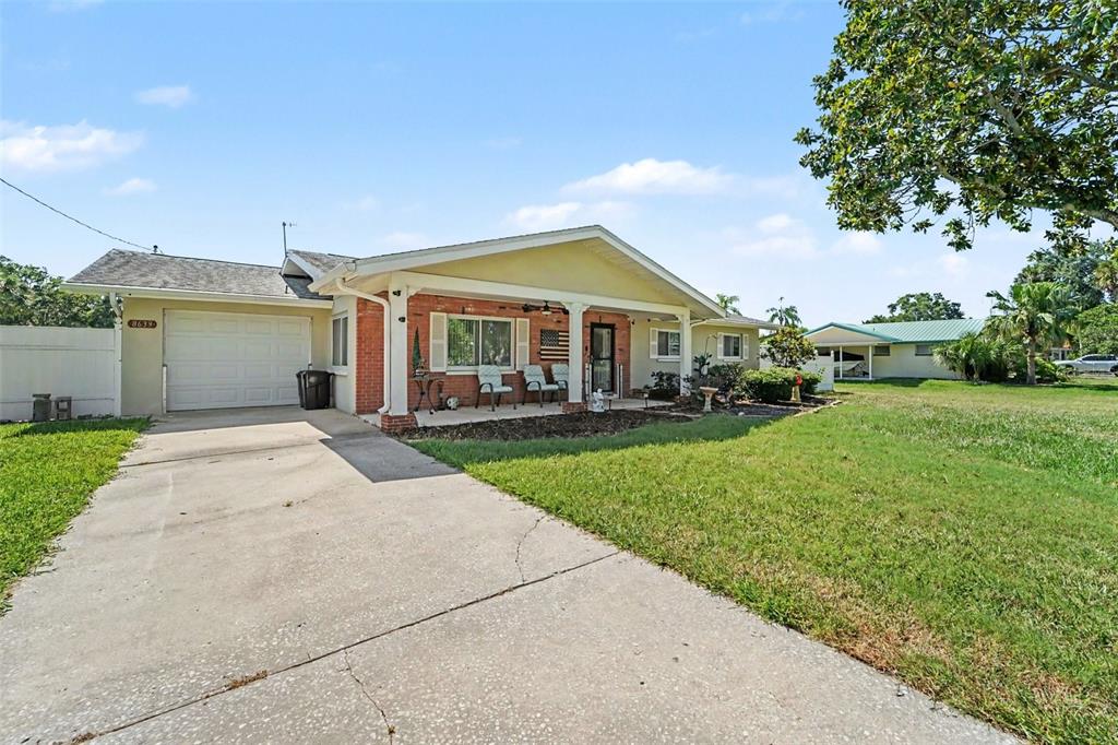 A single-story house with a brick facade, covered porch, and concrete driveway under a blue sky — 8639 GREEN STREET, PORT RICHEY, FL