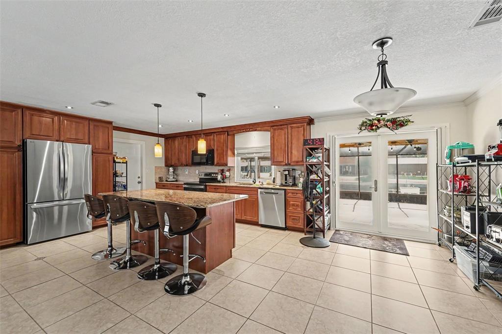 A kitchen features wood cabinets, granite countertops, a center island with stools, and tile flooring — 8639 GREEN STREET, PORT RICHEY, FL