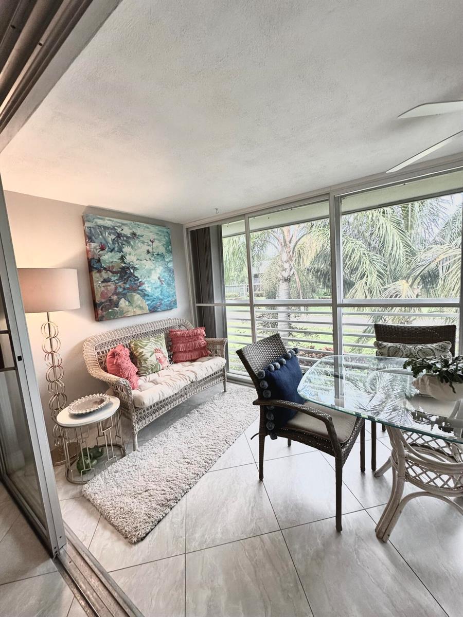 A sunroom features a wicker sofa, glass dining table, tile flooring, and large screened windows — 6 GARDEN Street # 204P, Tequesta FL 33469, TEQUESTA, FL