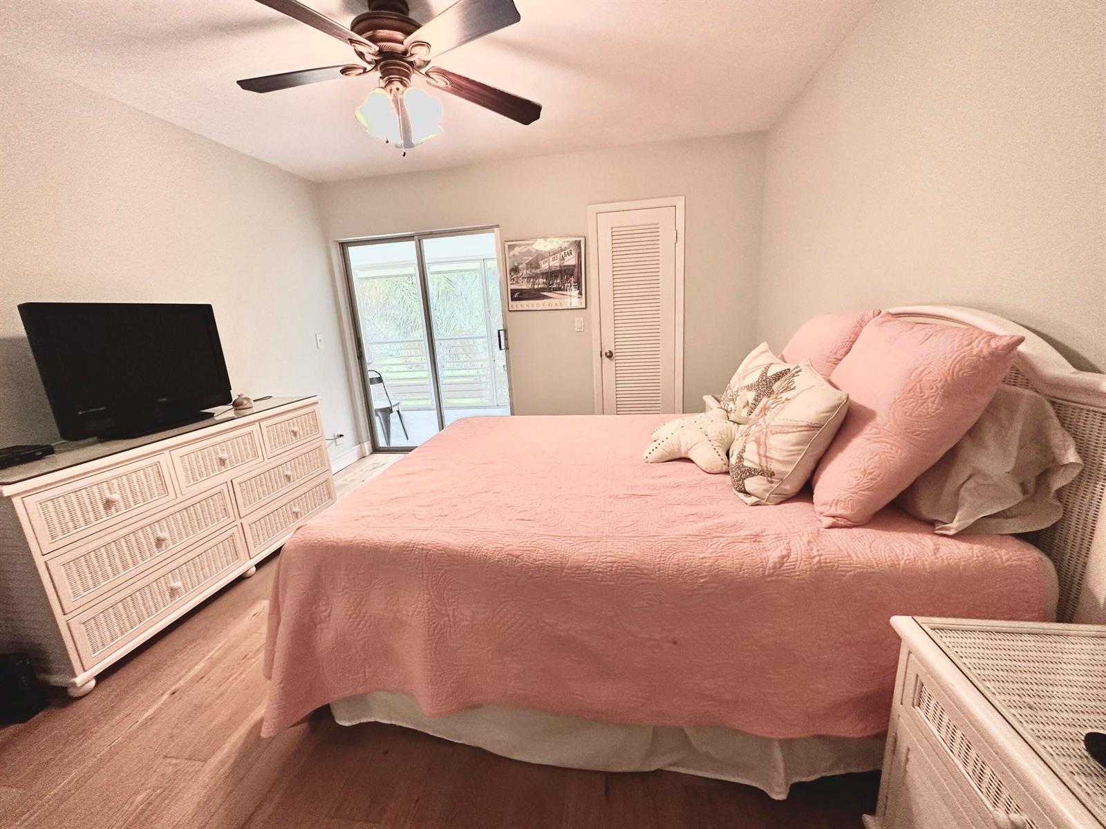 A bedroom with a pink bedspread, white wicker furniture, and a sliding glass door — 6 GARDEN Street # 204P, Tequesta FL 33469, TEQUESTA, FL