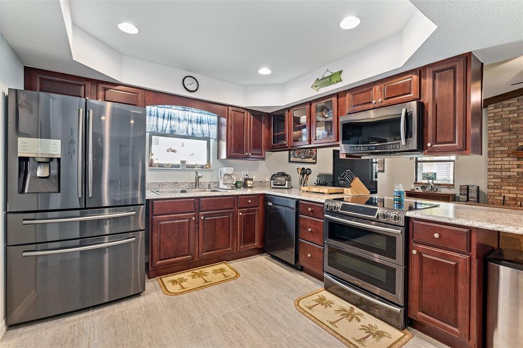 A kitchen features dark wood cabinets, stainless steel appliances, granite countertops, and tile flooring — 2008 N DAYTONA AVENUE, FLAGLER BEACH, FL