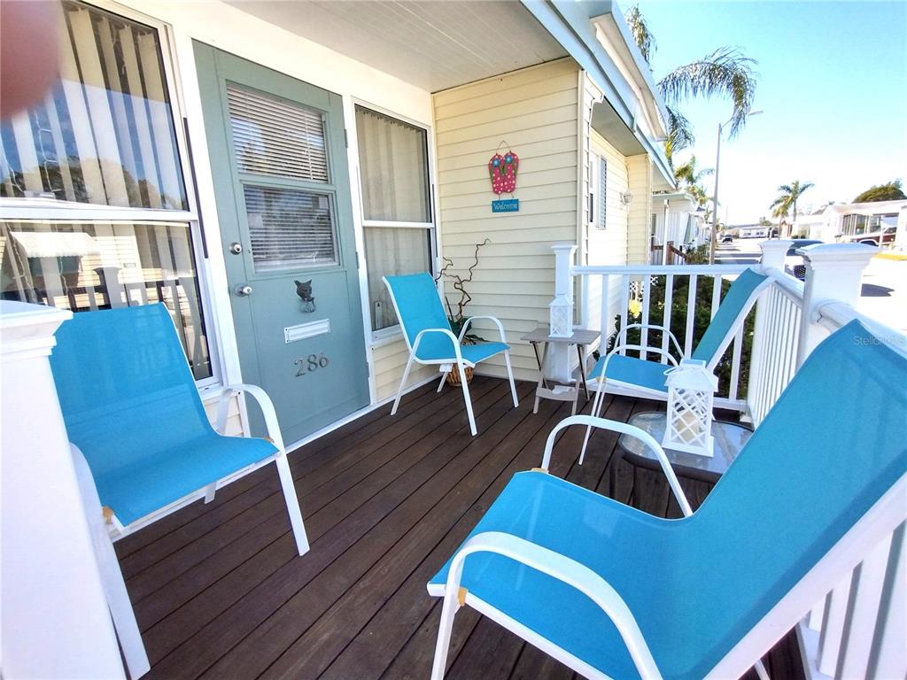 A wooden porch features three blue chairs, a small table, and a light green door — 82286 2ND AVENUE N UNIT 286, PINELLAS PARK, FL