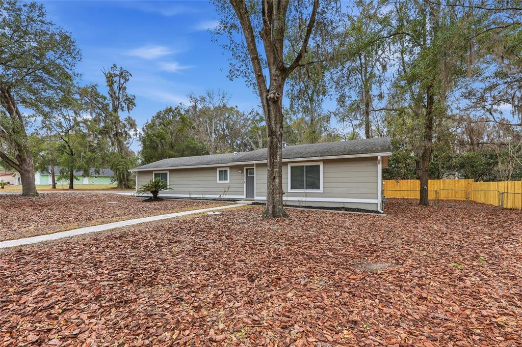 A single-story house with tan siding and a gray roof sits on a leaf-covered lot — 1656 NW 31ST PLACE, GAINESVILLE, FL