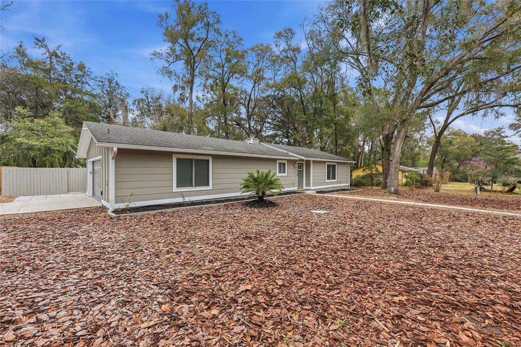 A single-story house with beige siding, a gray roof, and a large yard covered in mulch — 1656 NW 31ST PLACE, GAINESVILLE, FL