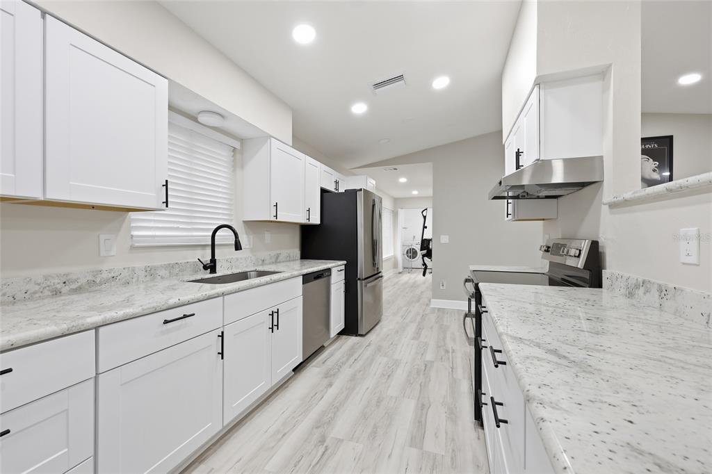 A kitchen features white cabinetry, granite countertops, stainless steel appliances, and light wood-look flooring — 1656 NW 31ST PLACE, GAINESVILLE, FL