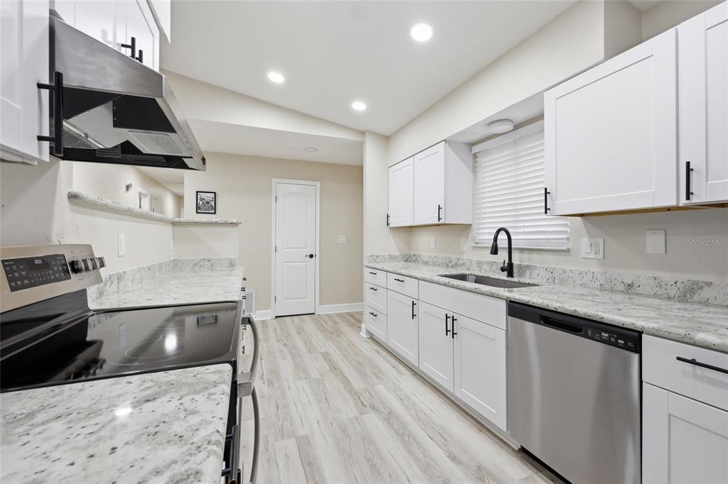 A modern kitchen features white cabinets, granite countertops, stainless steel appliances, and light wood flooring — 1656 NW 31ST PLACE, GAINESVILLE, FL